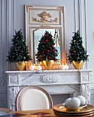 Three small Christmas tree from buxbaum on mantelpiece with lit candles by side