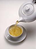 Grüner Tee wird aus weißer Teekanne in eine weiße Teetasse gegossen