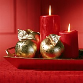 Rote dicke Kerzen und goldene Äpfel stehen in Schale mit Preiselbeeren