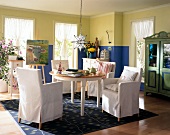 weiße Stuhlsessel am runden Tisch im Wohnraum mit blau/grüner Wand