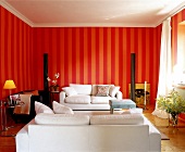 Wohnzimmer mit gestreifter Wand in rot und orange, weiße Sofas