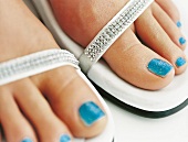 Extreme close-up of woman's feet wearing blue glitter nail paint and sandals