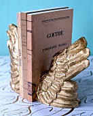 Close-up of bookends in form of golden angel wings between notebooks