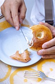 Ein Bagel (Brötchen-Ring) wird mit Butter bestrichen (close-up)