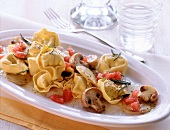 Tortellini with fried mushrooms and artichokes on oval plate
