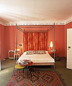 Himmelbett aus Eisen vor orangerot gestrichener Wand