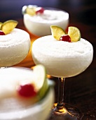 Four glasses of frozen daiquiri cocktail garnished with cherry and lemon slices, close-up