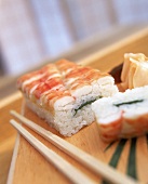 Sushi: 2 Stücke Oshi-Sushi Ebi liegt auf Holzbrett, daneben Holzstäbchen