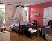 Ländlich romantisches Schlafzimmer, Eisenbett mit Moskitonetz, rote Wand