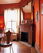 Zimmer mit Kamin u. Boden in dunklem Holz, rote Wände, Spiegel
