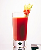 Glass of red vegetable juice garnished with halved tomato and celery