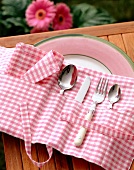 Cutlery and napkin arranged in pink gingham cutlery bag on plate