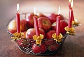 Ein Drahtkorb mit Äpfeln, geschmückt mit Kerzenhaltern und 5 Kerzen