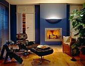 Living room with fireplace, black leather chair and wall lamp with dark blue wall