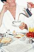 Mann im Bademantel am Frühstückstisch läßt sich Kaffee einschenken