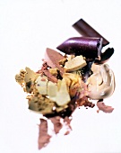 Make-up products in gold, pink and aubergine red smeared on white background