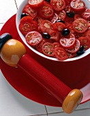 Roter Platzteller mit einer Schale Tomatensalat und einer Pfeffermühle