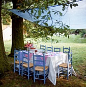 8 Stühle um einen Tisch im Garten gruppiert, darüber ein Sonnensegel