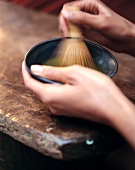 In einer Tasse wird mit einem Bambus pinsel Teepulver mit Wasser verrührt