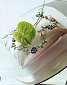 Kissen mit einer Blumenranke aus Perlen und Pailletten bestickt.