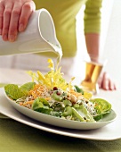 Close-up of woman's hand pouring leek sauce on lettuce and celery spring salad
