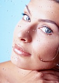 Close-up of beautiful blue eyed woman leaning on glass with water droplets