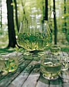 Waldmeisterbowle und Gläser auf einem Holztisch im Wald