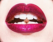dunkel violett geschminkter Frauenmund, Gewürznelke zwischen Zähnen