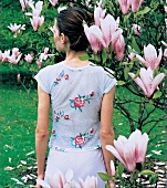 Frau in transparentem Top mit Blüten -stickerei steht am Magnolienbaum