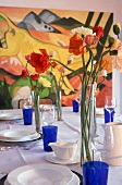 gedeckter Tisch, blaue Gläser,weißes Geschirr,in der Vase steht Mohn