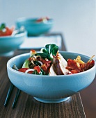 Bowl of marinated sesame chicken with bok choy and shoots in chilli sauce