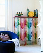 Radiator cover with colourful beaded curtain and modern chair with hand bag