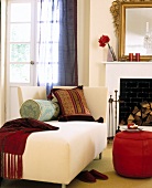 Cushions on long chair with red pouf in front of fireplace