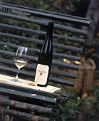 Glas und Flasche Weißwein aus dem Elsass stehen auf einer Parkbank