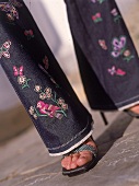 Frau trägt Jeans mit Minifransen und Stickerei am Saum,close up