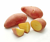 Two whole and one sliced sweet potato on white background