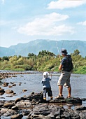 Vater und Kind stehen angelnd am Fluß, Rückenansicht
