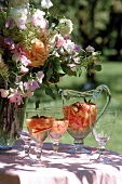 1 Karaffe und 2 Gläser mit Maibowle stehen neben Blumenstrauß  auf Tisch