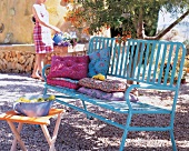 Türkisfarbene Eisen-Gartenbank mit dicken Blumenkissen unterm Baum
