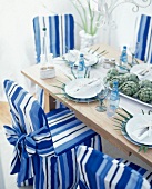 Stühle mit blau-weiß gestreiften Hussen an gedecktem Tisch