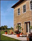 Schlichte Terrasse vor Holzhaus, mit Pflanzenkübeln und Holzmöbeln