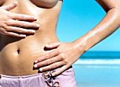 Close-up of woman rubbing hands on tanned bare stomach on the beach