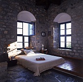 Doppelbett mit weißer Überdecke in schattigem Zimmer mit Steinmauern