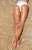 Frauenbeine am Strand im Wasser Bikinihose in weiß