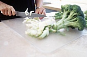 Close-up of man's hands slicing onions and broccoli on an acrylic board