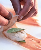 Close-up of man's hands wrapping filet with sage leaf in ham