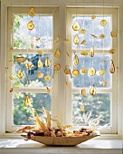 Fensterschmuck: Getrocknete Fruchtscheiben an Bändern vor dem Fenster