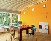 Maisgelber Raum mit Stäbchenparkett: massiver Tisch + farbige Stühle