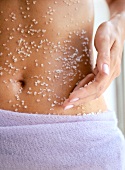 Close-up of woman rubbing sea salt to her belly, mid section