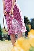 Woman wearing floral pattern dress watering flowers with hose in garden
